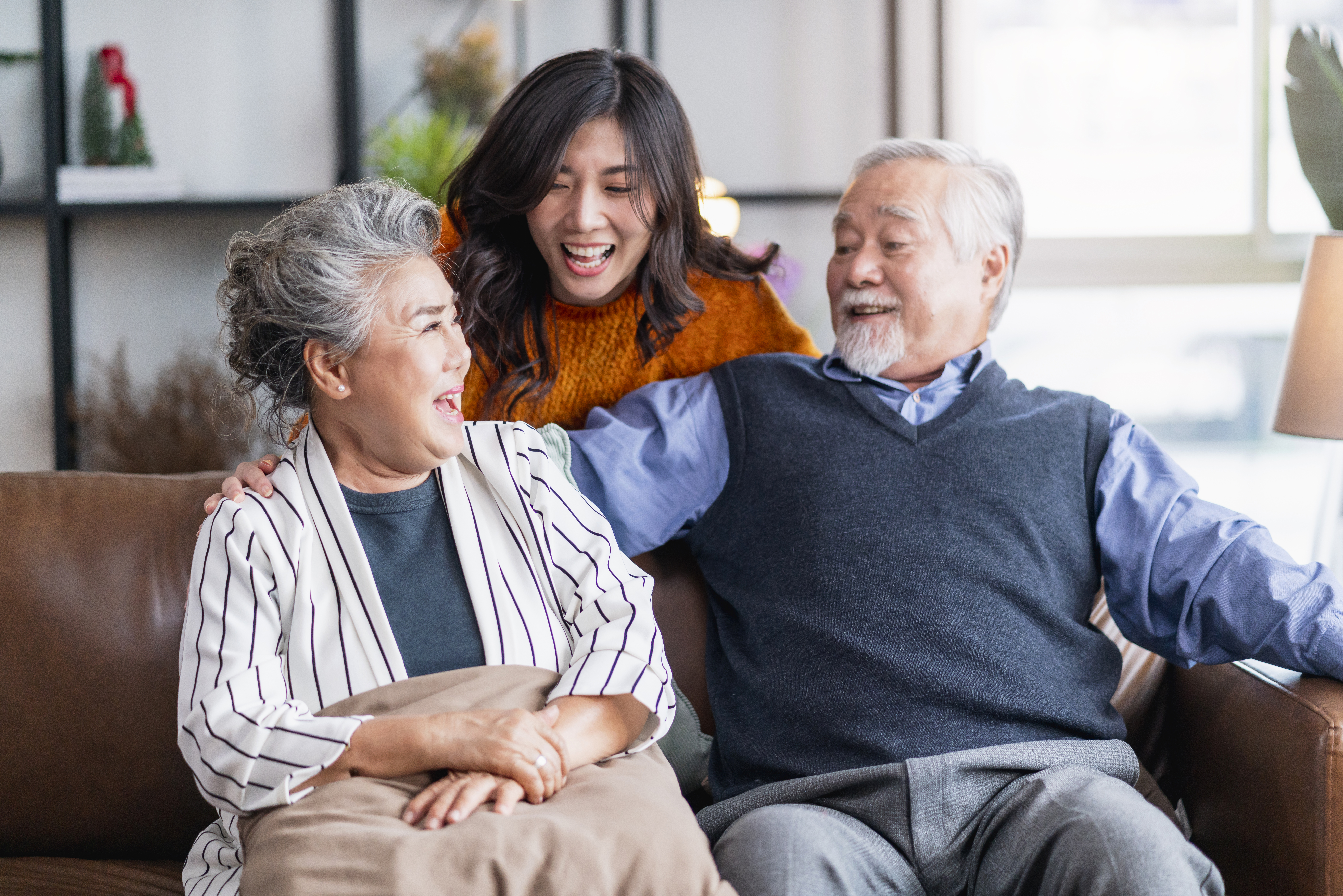 old happy asian couple laughing with their daughter sitting on a sofa